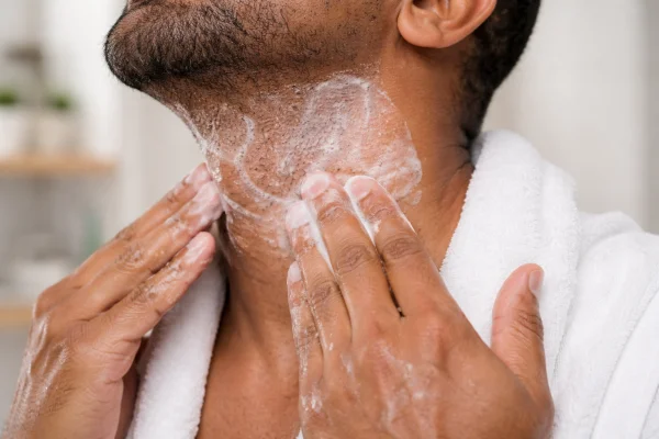 A person cleansing the neck area with a gentle skincare product in a bathroom setting.